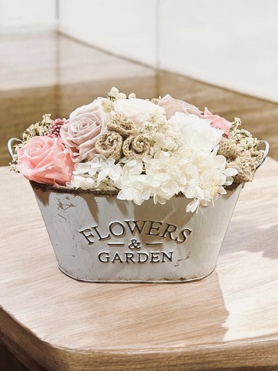 A white planter with flowers in it on top of a table.