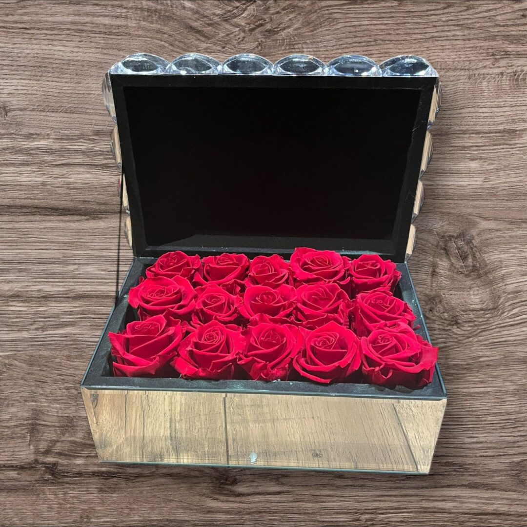 A box of red roses on top of a wooden table.