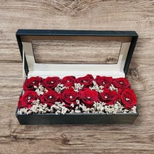 A box of red roses on top of a wooden table.